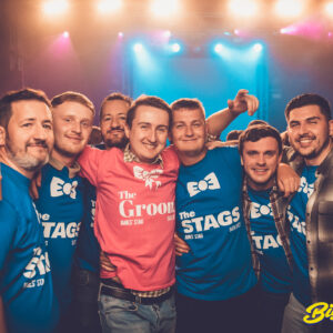 A stag due in blue and pink shirts, smiling towards the photographer