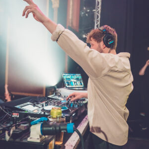 DJ in a white shirt has one arm in the air.